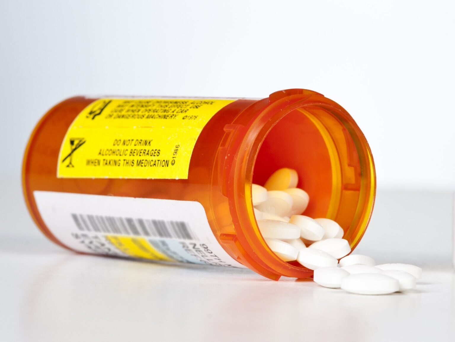An orange prescription bottle on its side with white tablets spilling out onto a white surface.