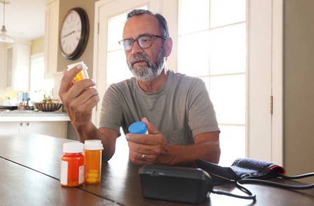 A man at his kitchen table sorting through prescription bottles.